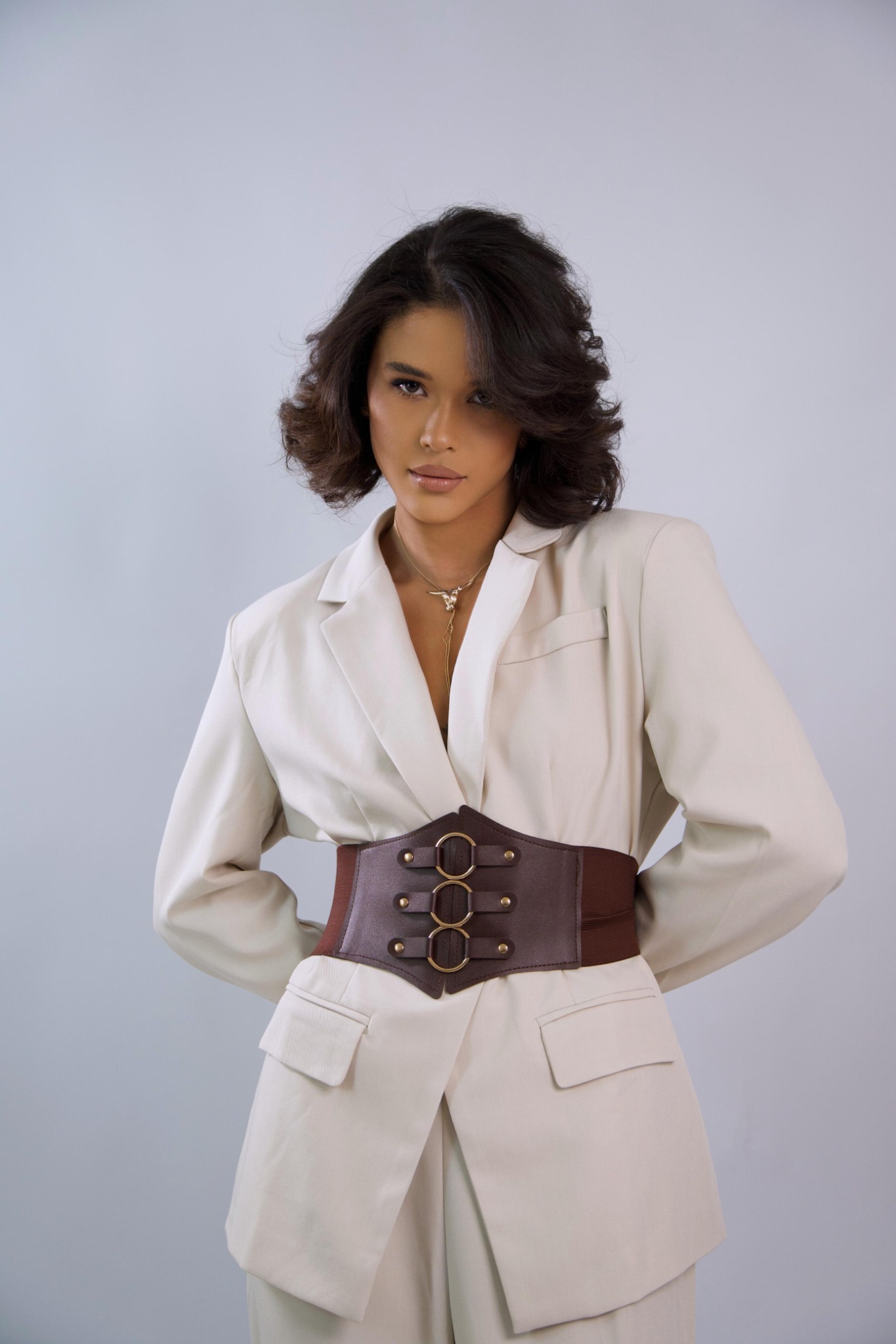 Iasmyne Sampaio com traje claro e cinto marrom, olhando para a câmera